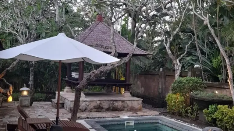 a pool with a bench and an umbrella and a table and chairs at The Royal Beach Seminyak Bali in Seminyak