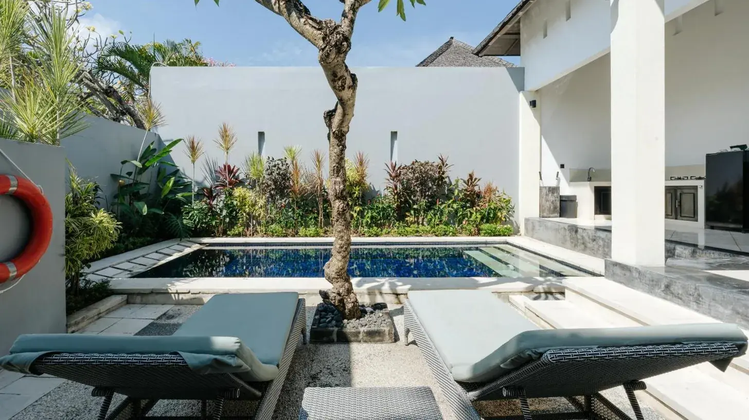 a pool in the backyard of a house with chairs and a tree at The Seminyak Suites Private Villas in Seminyak