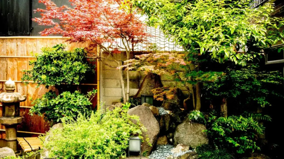 a garden with rocks and trees and a fence at Udatsuya in Osaka