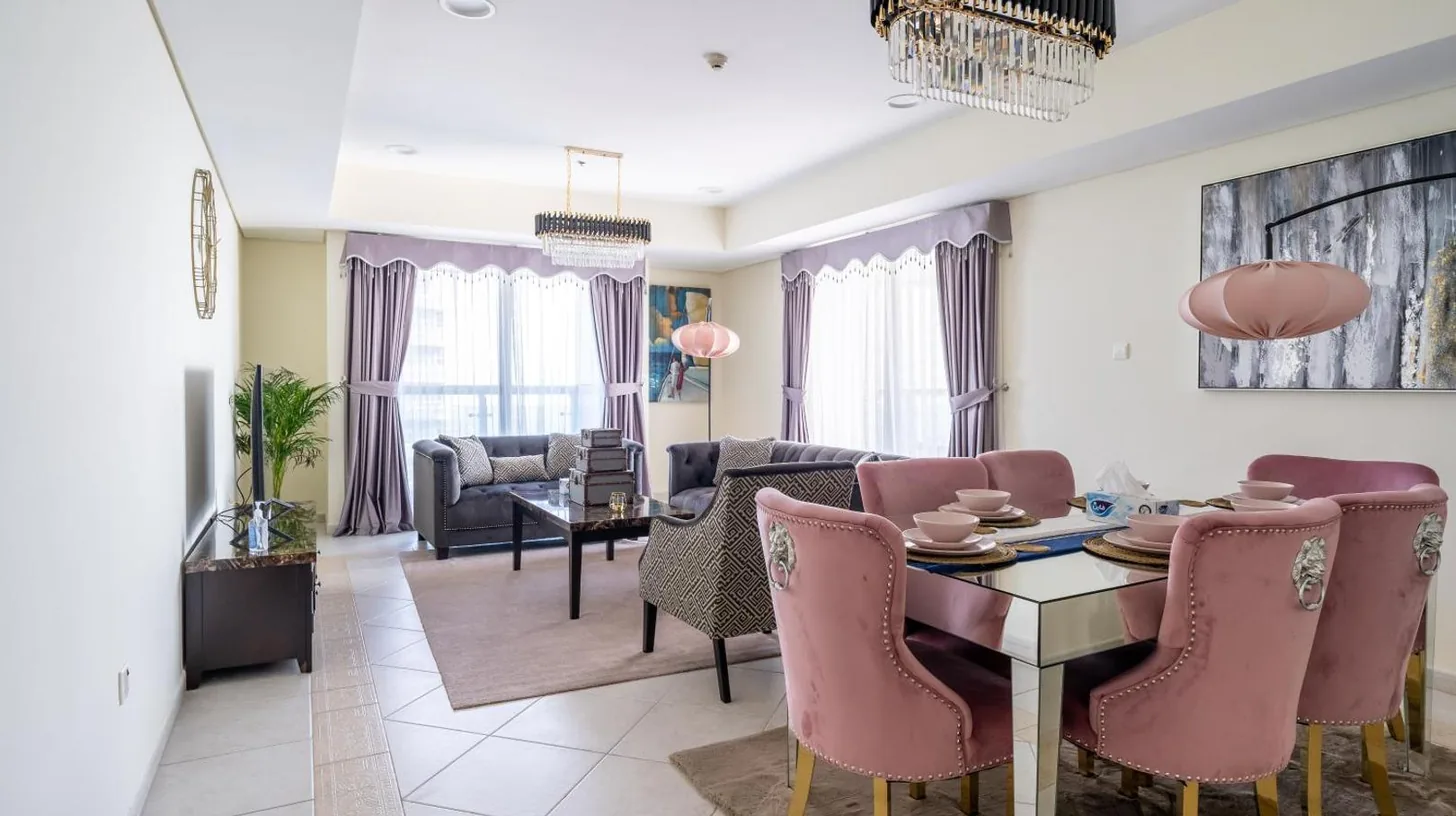 una sala de estar con una mesa de comedor y sillas rosas en Veer Apartments - 82nd Floor Princess Tower - Palm View en Dubái
