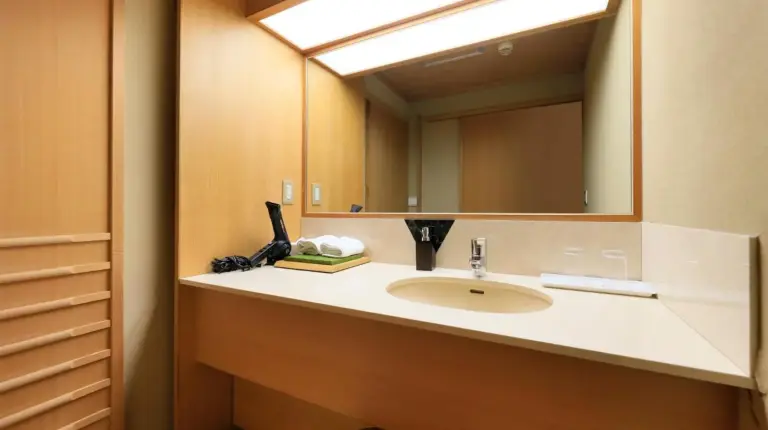 une salle de bain avec un lavabo et un grand miroir au Wakamatsu Hot Spring Resort à Hakodate